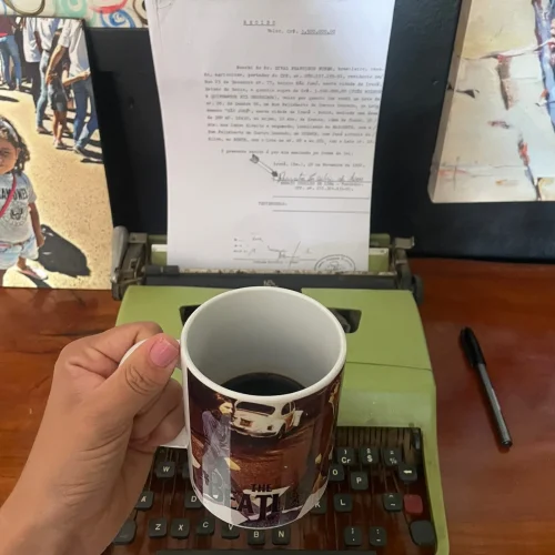 Uma pessoa segurando uma xícara de café de frente para uma máquina de escrever com um texto expresso