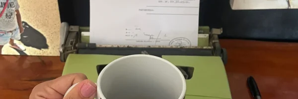 Uma pessoa segurando uma xícara de café de frente para uma máquina de escrever com um texto expresso