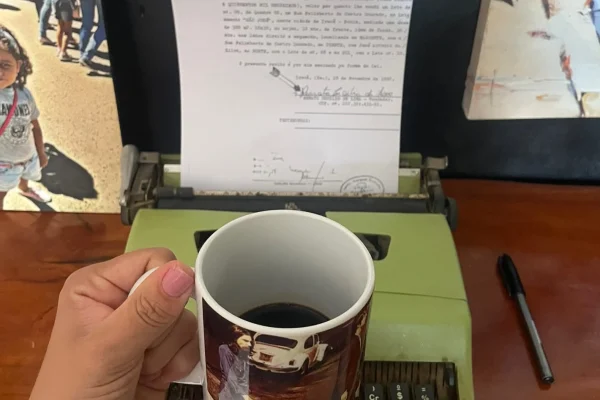Uma pessoa segurando uma xícara de café de frente para uma máquina de escrever com um texto expresso